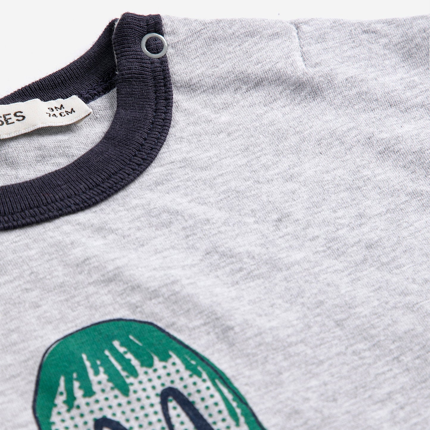 Gray shirt with green dinosaur design and navy collar, brand label visible.