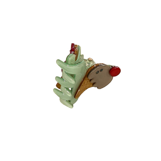 Decorative hair clip with a green base, red accents, and a small animal figure on a beige surface.