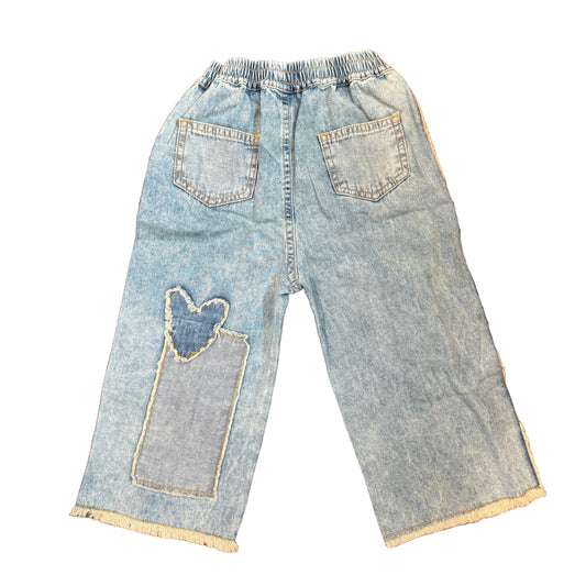 Pair of light blue jeans with patches on a wooden surface