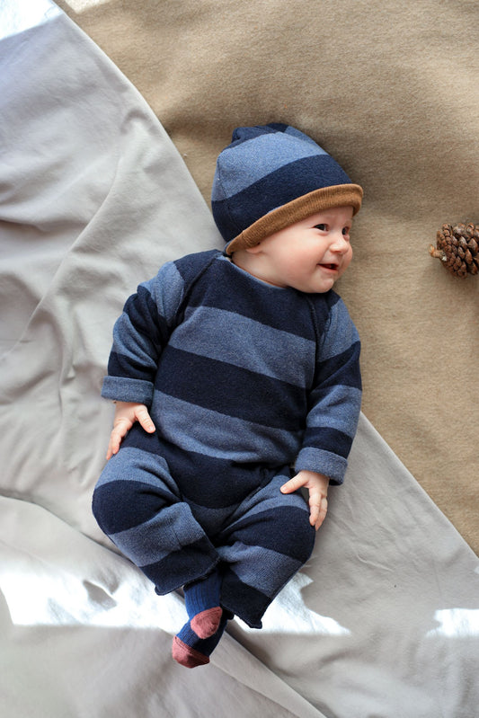 Baby wearing a blue striped outfit and hat lying on a textured surface