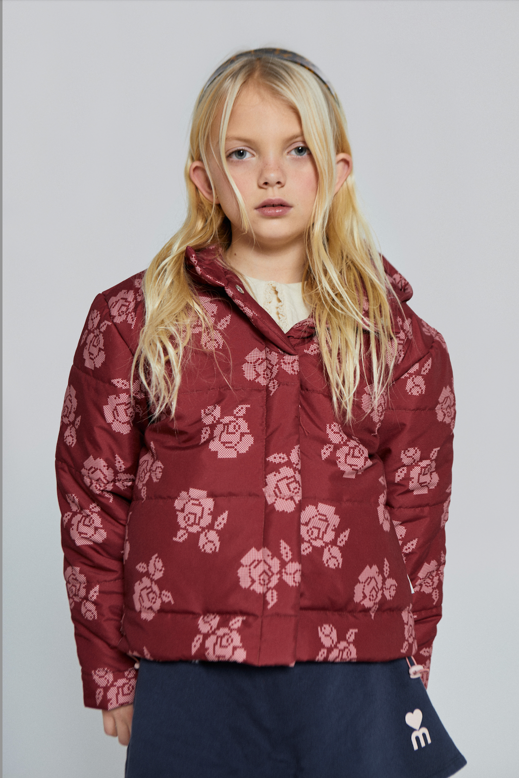 Young girl wearing a red floral puffer jacket with cross-stitch flower print