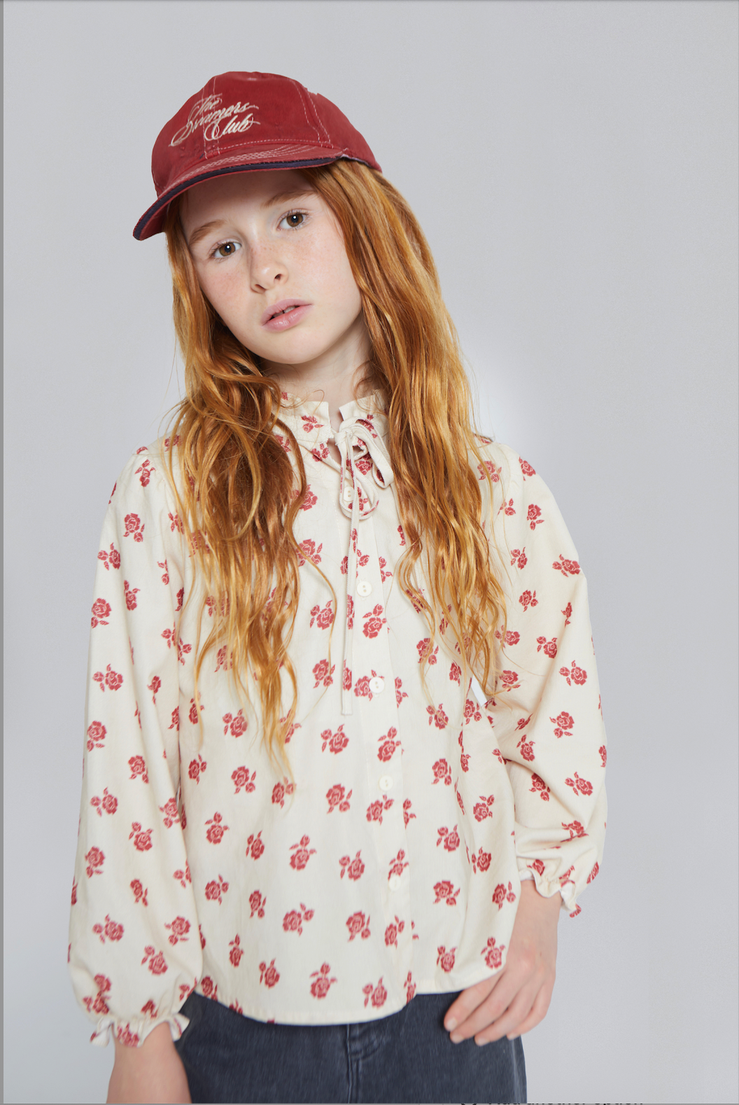 Young girl wearing a red cap and floral blouse against a plain background