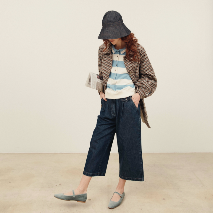 Person wearing a striped shirt, plaid jacket, and wide-leg jeans in a minimal setting.