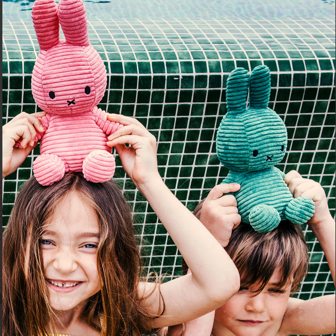 Two children holding pink and green plush toys by a pool.