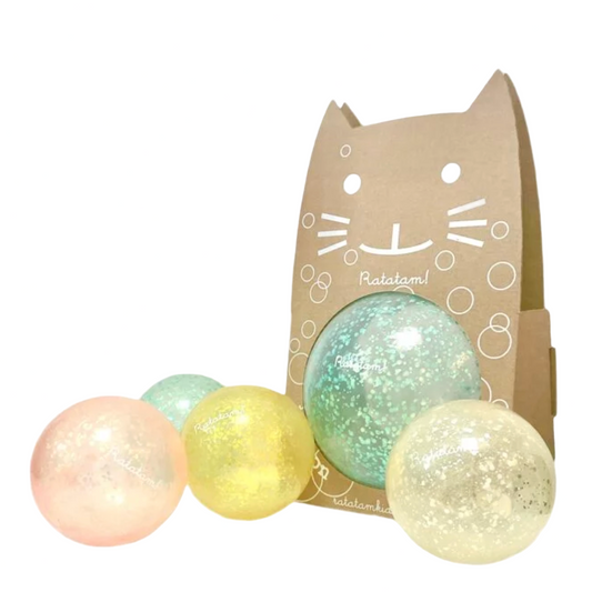 Three glittery balls in pastel colors with a cardboard box featuring a cat design on a white background.
