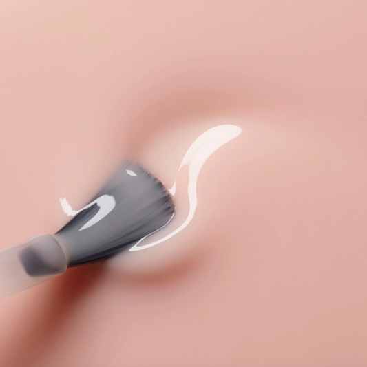 Close-up of a makeup brush applying cream to skin with a blurred background