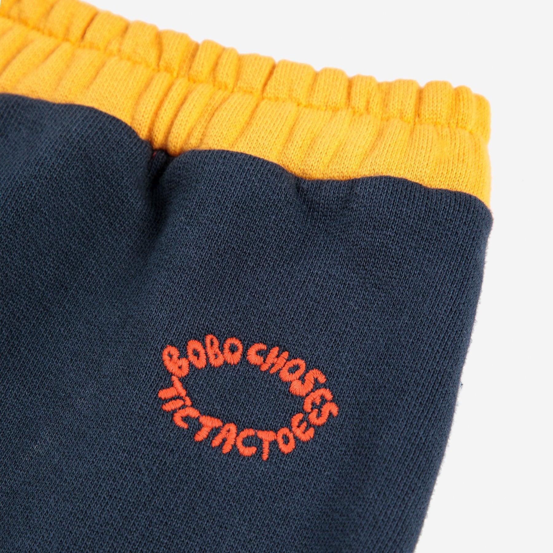 Navy sweatpants with orange waistband and embroidered text on a white background