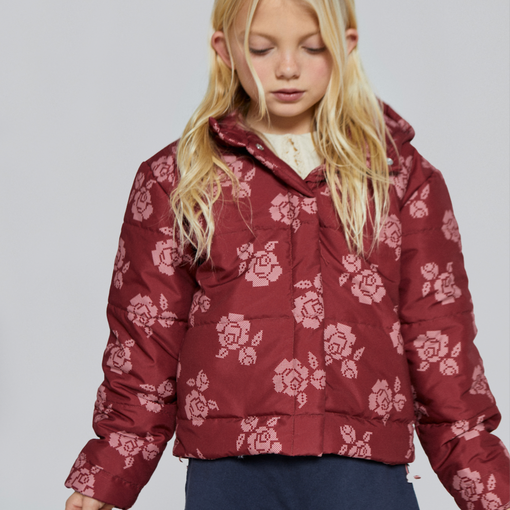 Young girl wearing a red floral puffer jacket with cross-stitch flower print