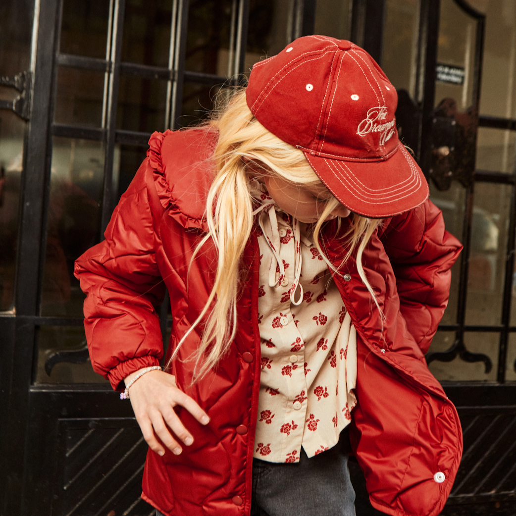 Person wearing a red puffer jacket and matching red cap in front of a black metal gate.