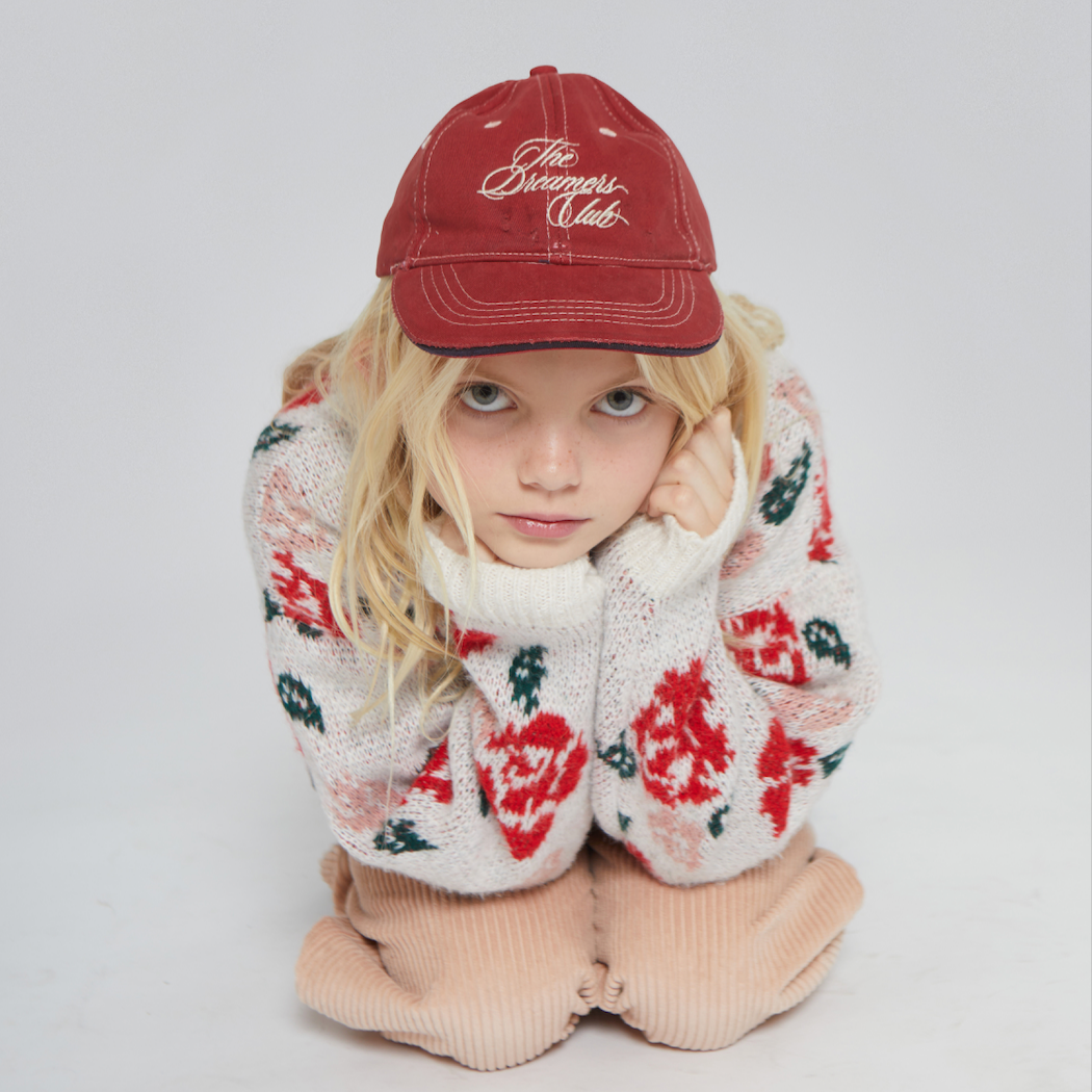 Person wearing a red cap and floral sweater on a light gray background