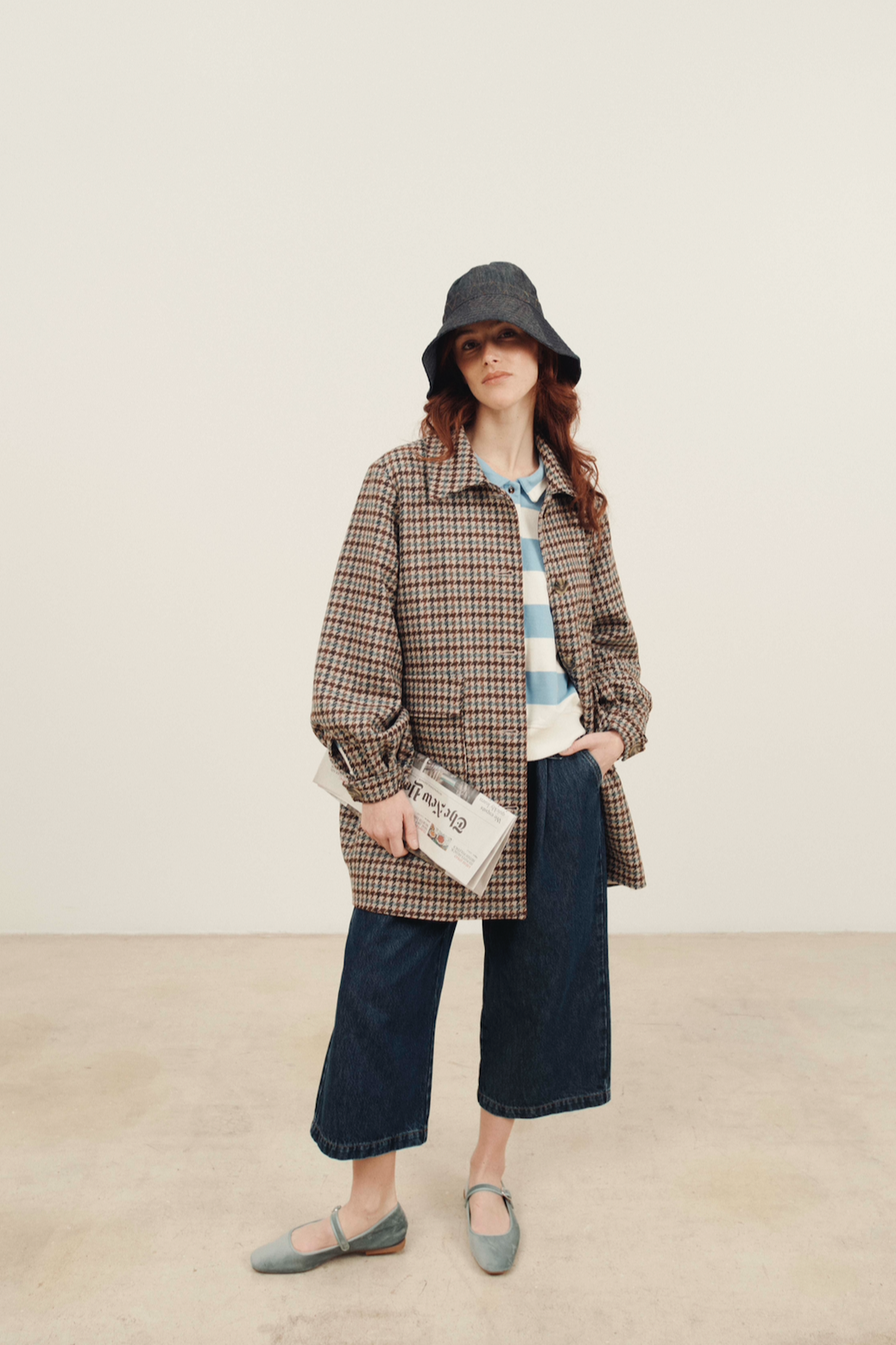 Person wearing a plaid coat, black hat, and dark jeans on a plain background