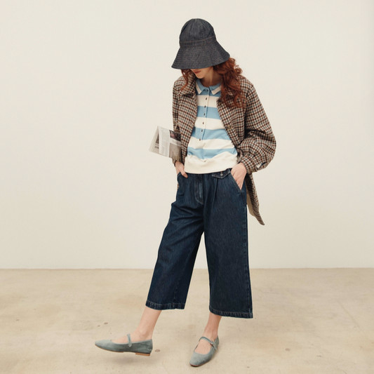 Person wearing a striped shirt, plaid jacket, and wide-leg jeans in a minimal setting.