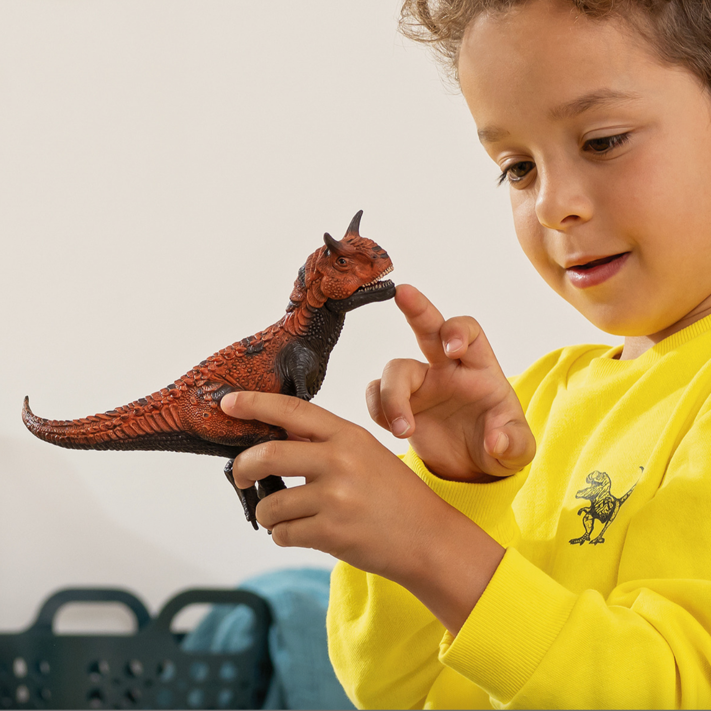 Child playing with a toy dinosaur figure, wearing a yellow shirt with a dinosaur design.