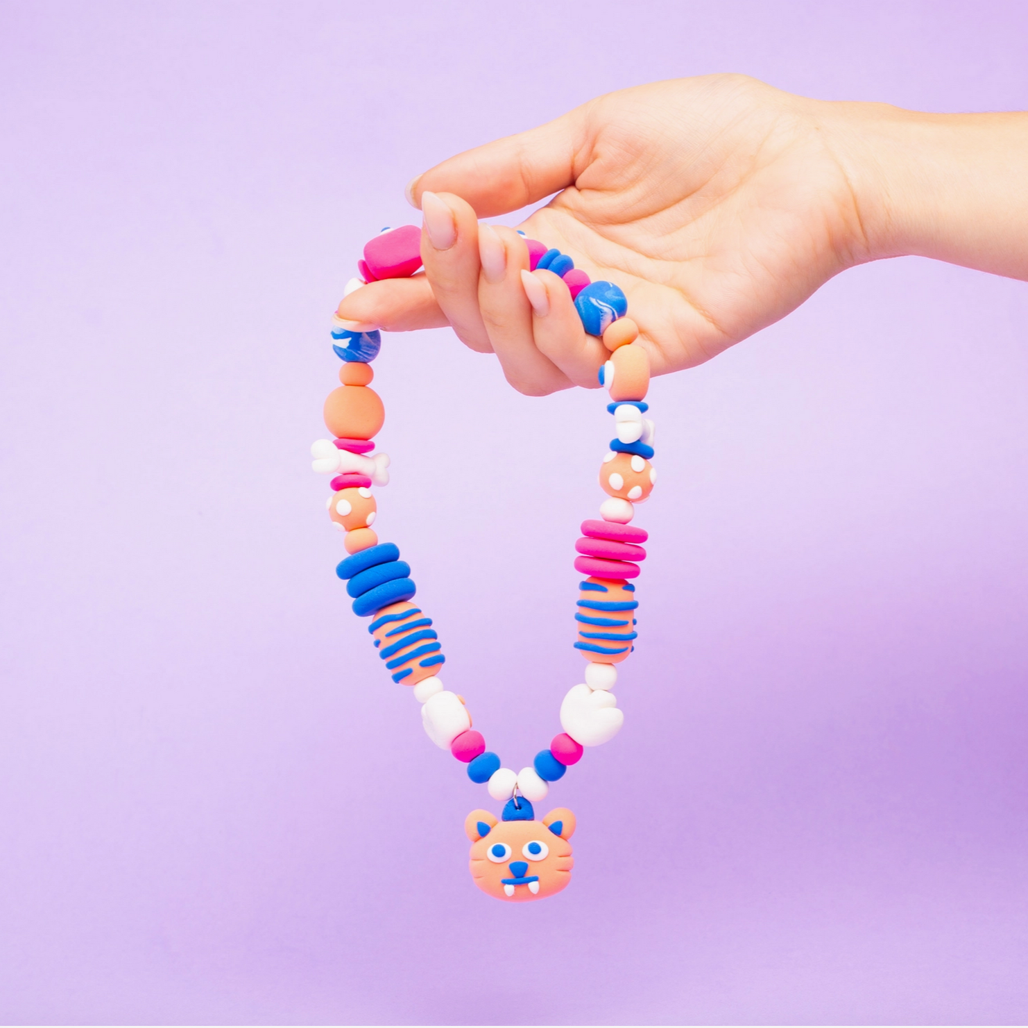 Colorful beaded necklace with a bear pendant held by a hand against a purple background