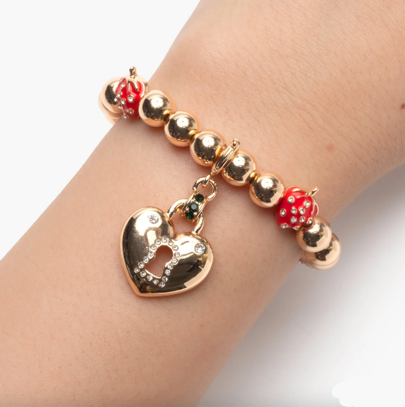Gold bracelet with heart charm and red beads on a wrist against a white background