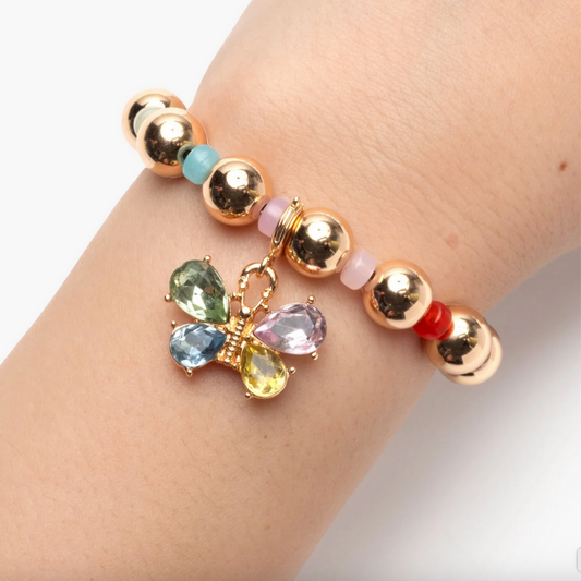 Gold beaded bracelet with a colorful butterfly charm on a wrist against a white background
