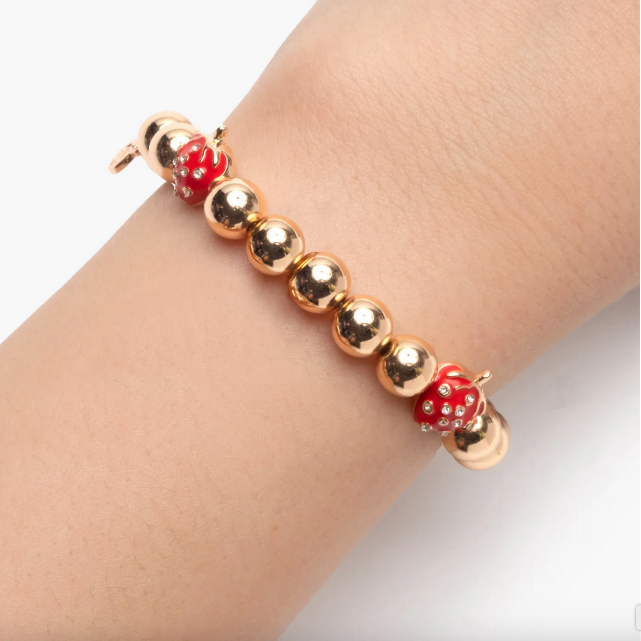 Gold bracelet with red dice-shaped charms on a wrist against a white background