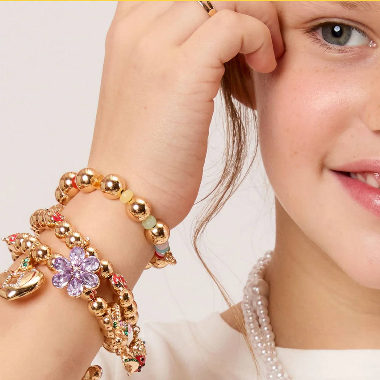 Close-up of a child's hand wearing a gold bracelet with colorful beads and a pearl necklace.