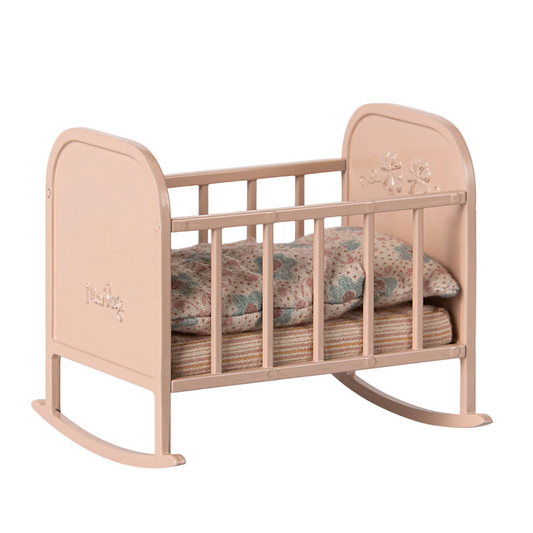 Pink baby crib with floral bedding on a white background