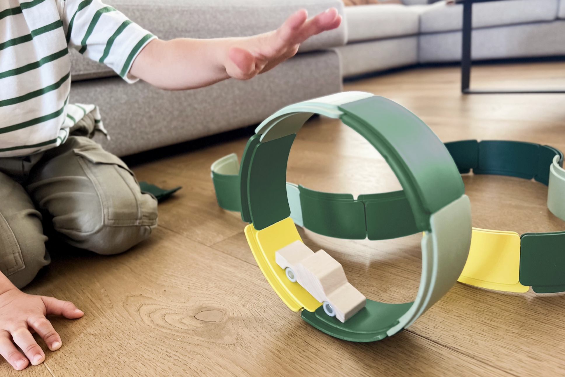 Child playing with a green and yellow toy track on a wooden floor.