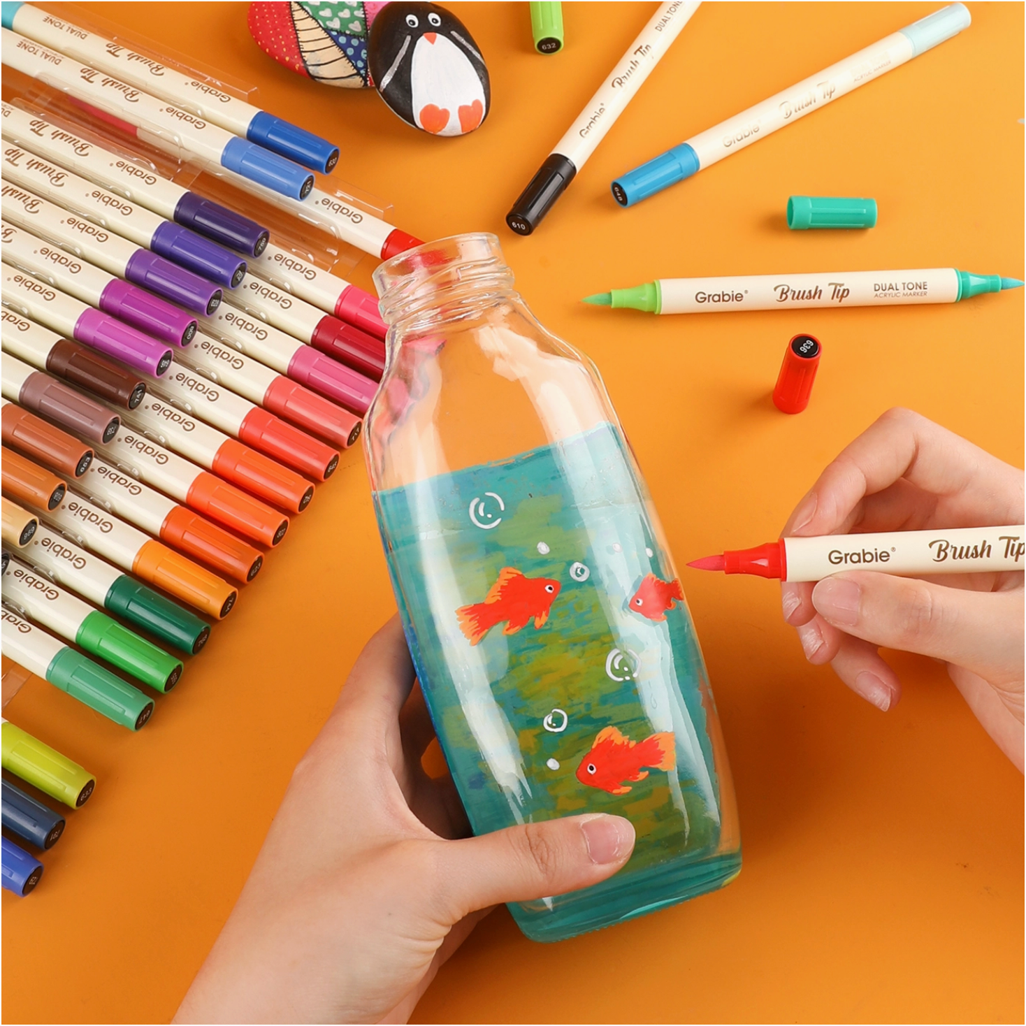 Colorful markers and a decorated bottle with fish illustrations on an orange background