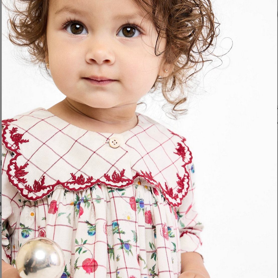 Child wearing a dress with a red lace collar and floral pattern, holding a silver ball.
