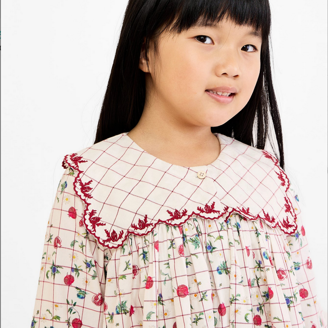 Young girl wearing a checkered dress with floral patterns on a white background