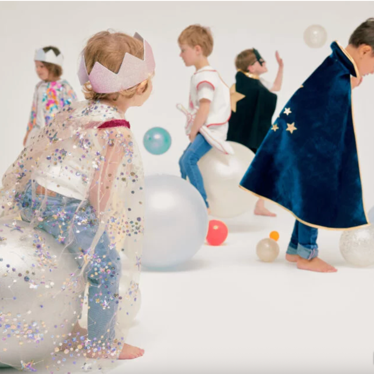 Children in costumes playing on a white floor with colorful balloons.