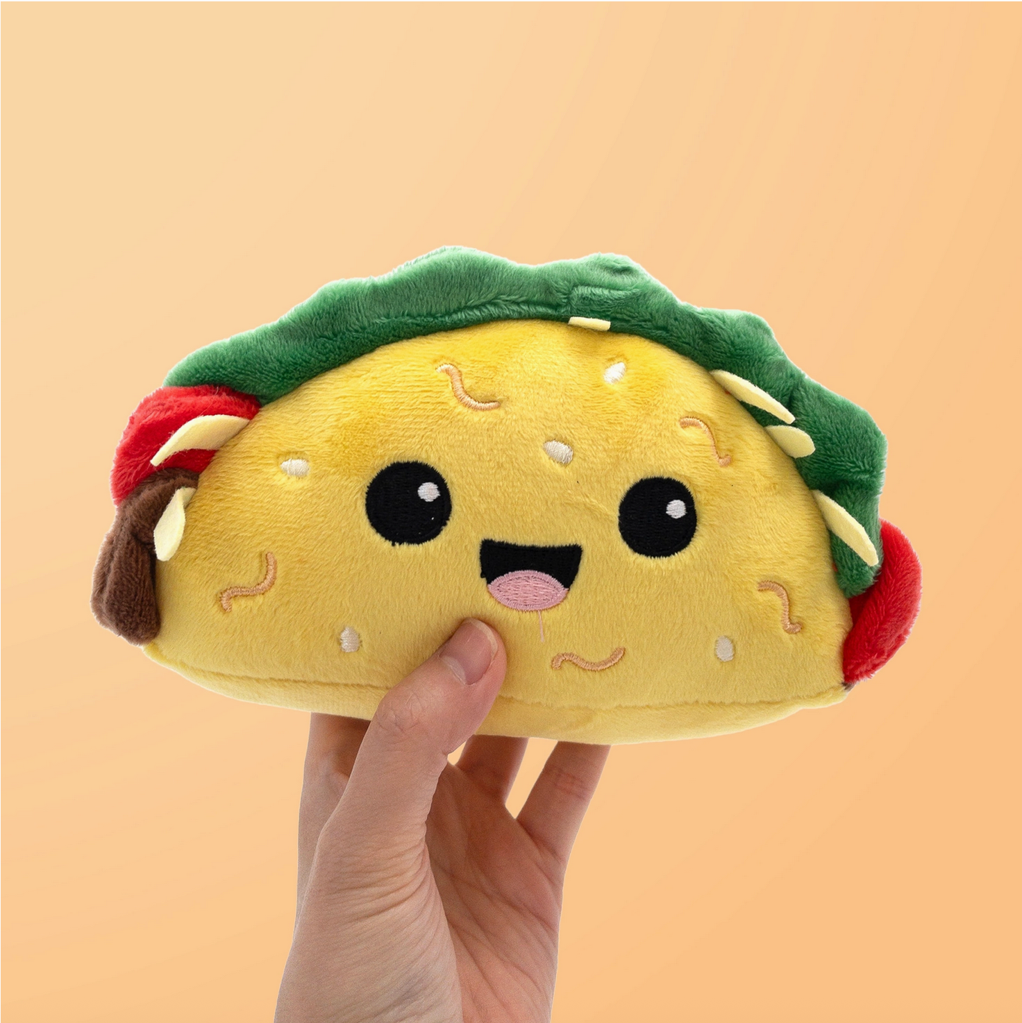 Plush taco toy held by a hand against a beige background