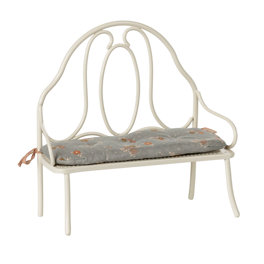 White metal bench with a floral cushion on a light beige background