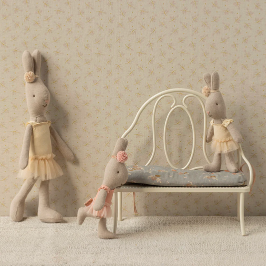 Three plush rabbit toys in a decorative setting with a bench and wallpaper.