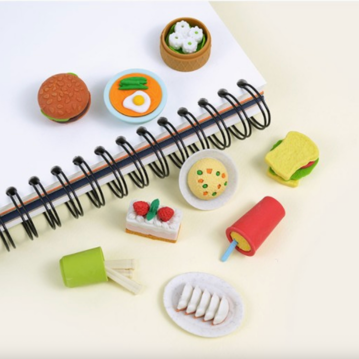 Miniature food items arranged around a notebook on a light background