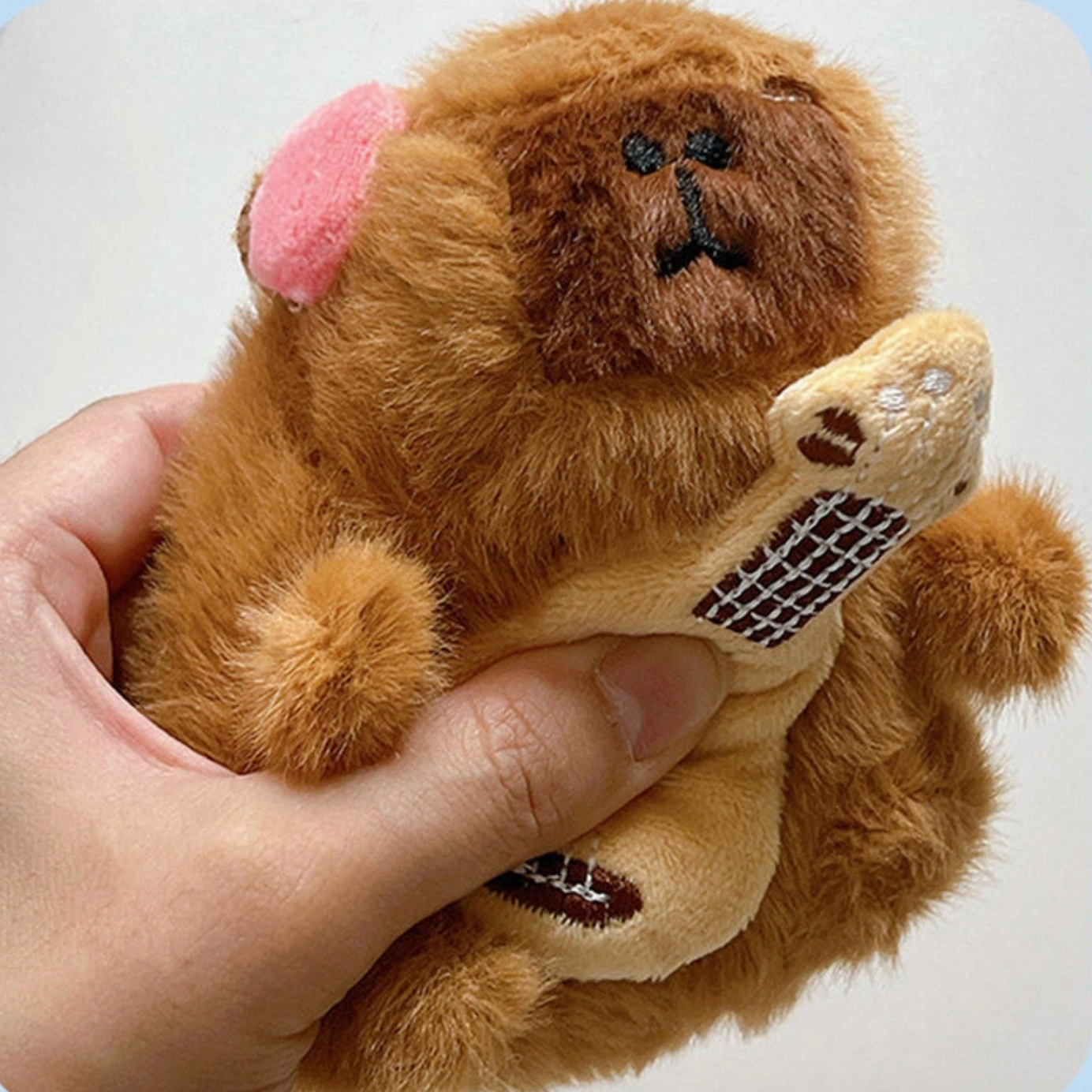 Plush monkey toy held in a hand against a light blue background