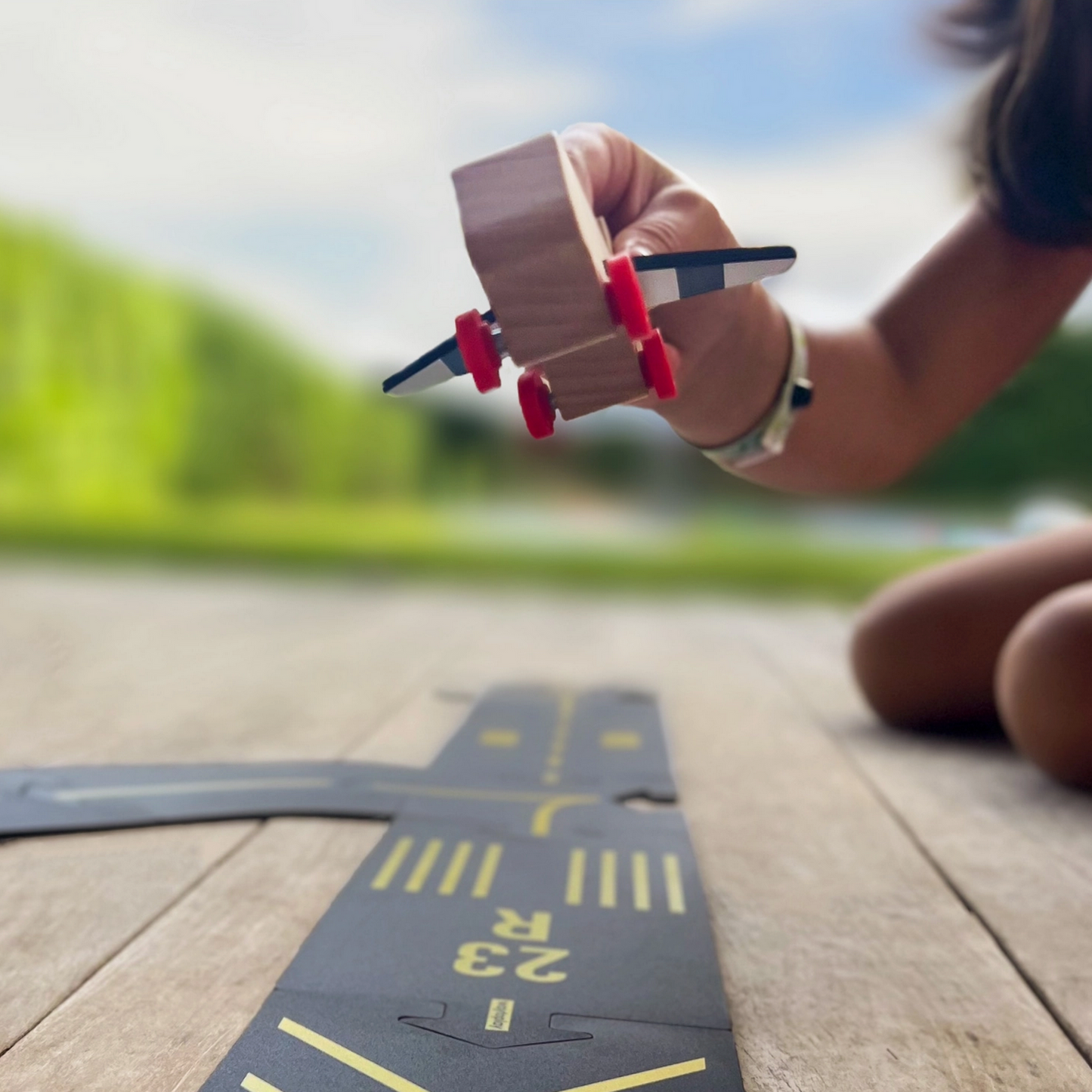 Person playing with a toy car on a wooden surface with a blurred natural background