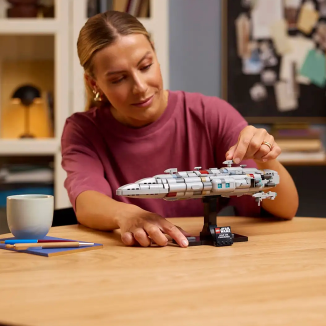 Woman assembling a model spaceship on a table with a cup and pens nearby.