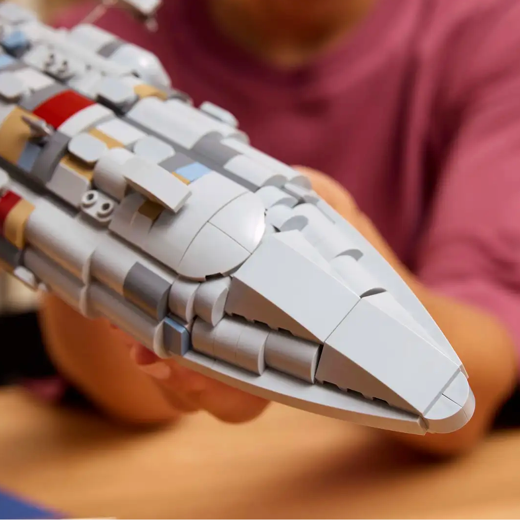 Person holding a detailed model of a spaceship, likely made from building blocks, with a blurred background.