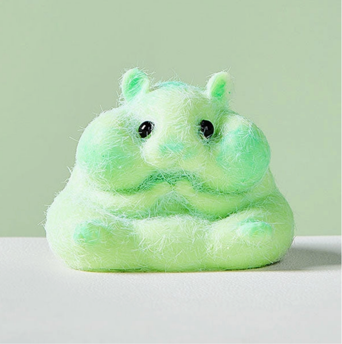 Light green plush toy resembling a hippo on a white surface with a light gray background